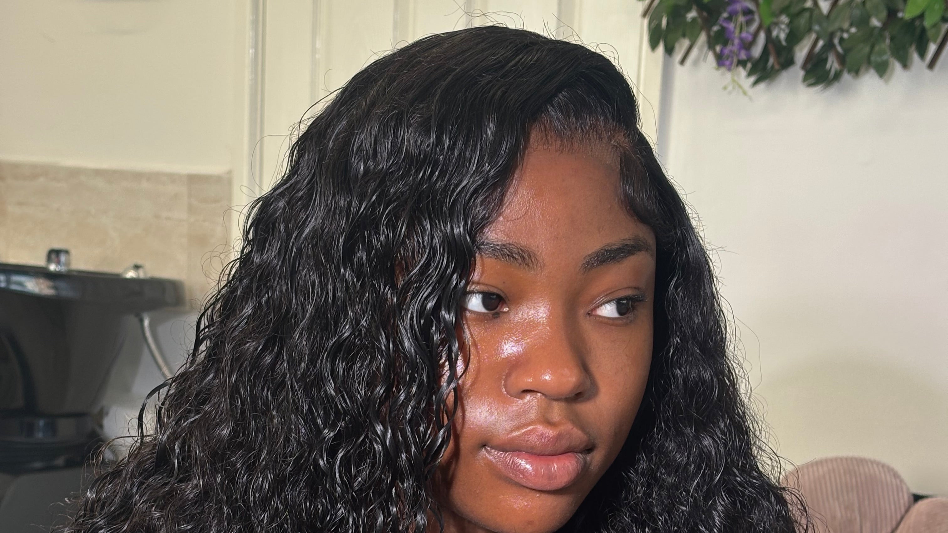 Person with long, curly hair standing indoors with a neutral background